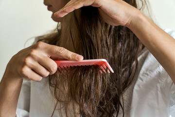 Beautiful woman brushing her wet messy hair after bath with comb. Thin hair porblem