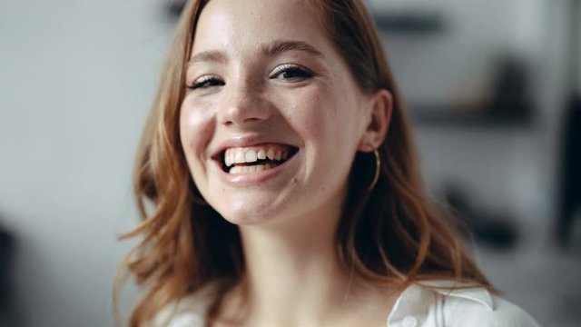 Cheerful good looking young redhead woman with freckles in the apartment looks at camera and smiles sincerely having fun