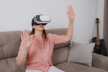 Woman using VR sitting on the couch with a sense of immersion in a virtual environment.