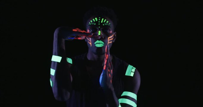 Studio, slow motion, close-up of a neon-painted dancer using elaborate hand gestures