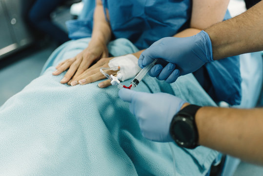 Crop female patient sitting with covered legs and intravenous fluid needle in hand before surgery in operating room