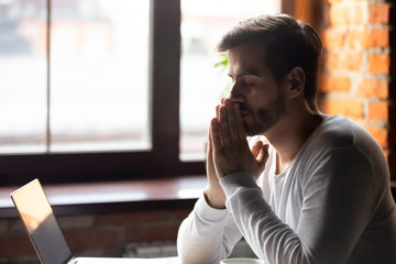 Worried man thinking about problem puts hands together in prayer
