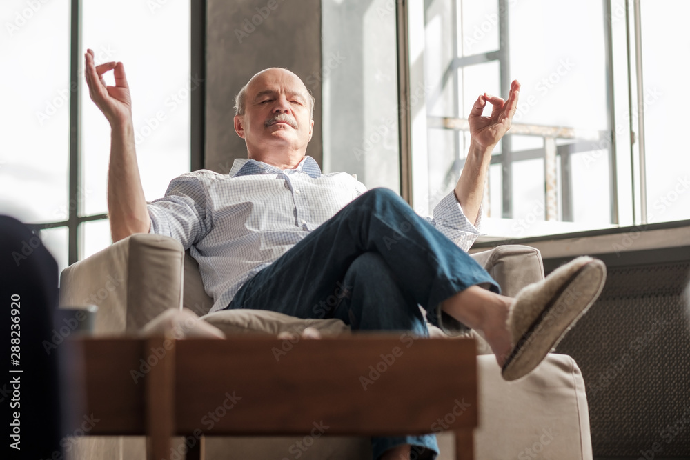 Wall mural senior hispanic man meditating on the sofa in the living room. stay calm during everyday troubles.