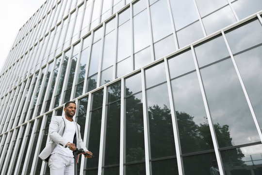 Black man in suit on electric scooter in business center