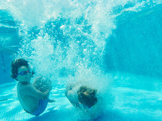 Cheerful playful boys jumping deep inside of clear pool water having fun