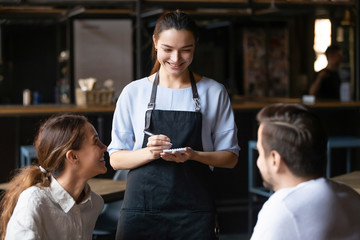 Young couple ordering food in cafe, smiling waitress serving customers