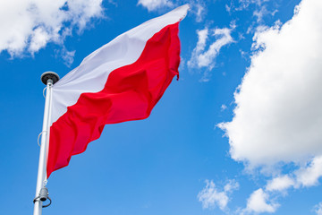Polish flag on a background of the cloudy sky. National symbol of Poland on the mast.