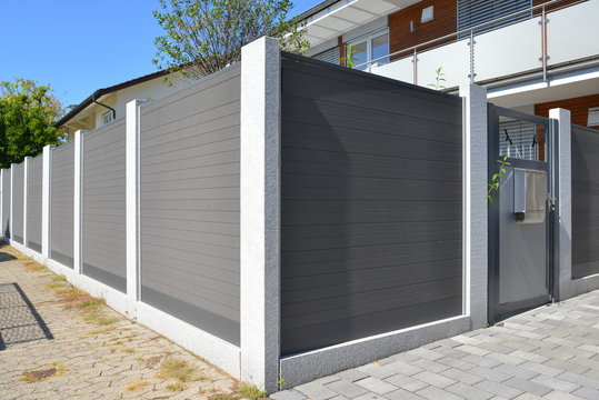 Hohe Sichtschutzwand aus Metall mit Eingangsbereich als Grundstücksabgrenzung vor einem Wohnhaus