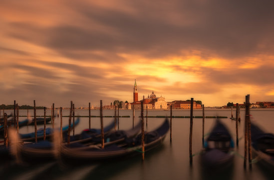 Pier with empty boats in water against fiery sunset and beautiful city with old towers and rooftops