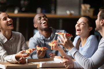 Diverse friends eating pizza and having fun together in cafe