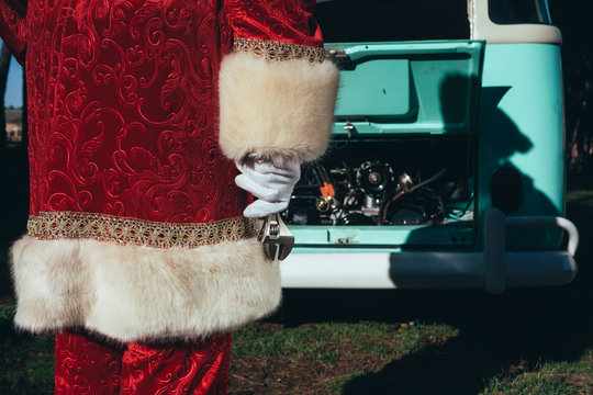 Unrecognizable person in red and white costume of Santa Claus inspecting engine of vintage green van on sunny day
