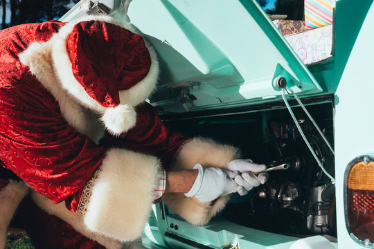 Unrecognizable person in red and white costume of Santa Claus inspecting engine of vintage green van on sunny day