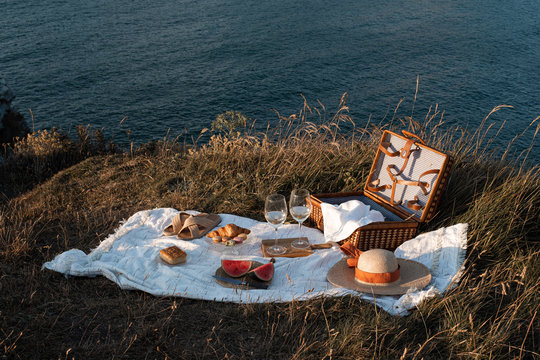 Picnic mat with romantically set with glass of drink and food on dry shore with serene water and hills