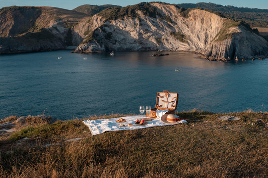 Picnic mat with romantically set with glass of drink and food on dry shore with serene water and hills