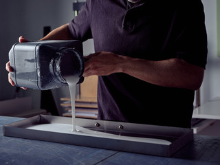 Bookbinder pouring glue into mold from square bottle