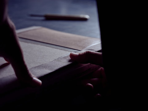 Crop man creating book hardcover gluing fabric on carton piece working at table