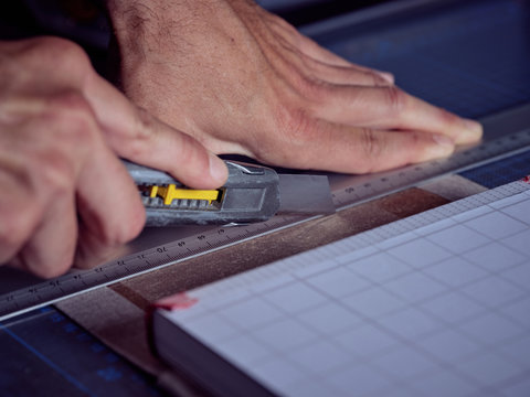 Faceless man working in bookmaking studio and measuring cover for book using pencil and ruler