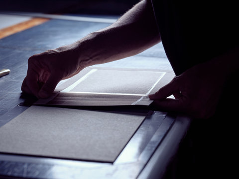 Crop man creating book hardcover gluing fabric on carton piece working at table