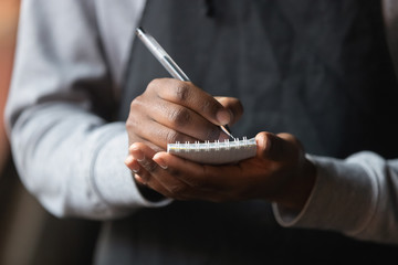 Close up African American waiter hands with notebook, taking customer order - Powered by Adobe