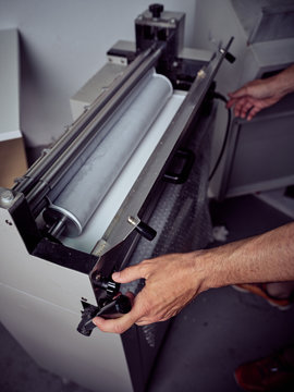 Crop unrecognizable employee working on modern gluing machine in printing office