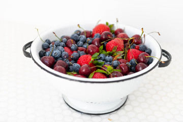Colander Filled with Various Berries in White Tile Sink