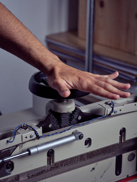 Crop hand of competent craftsman rotating handle wheel of binding press machine on blurred background
