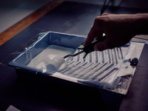 Crop unrecognizable worker dipping paint roller in glue bowl for printing books