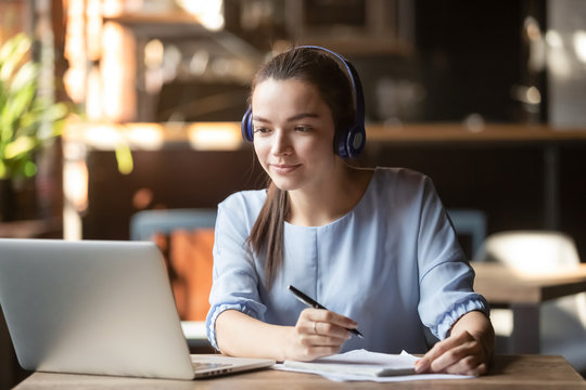 Focused woman wearing headphones using laptop, writing notes