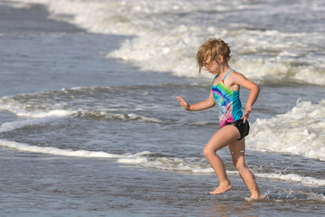 Young girl running from ocean wave