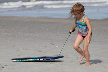 Young girl dragging boogie board in the sand