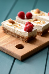 Vegan low calorie dessert. Coconut milk cheesecake bars decorated with raspberries and coconut flakes on wooden board
