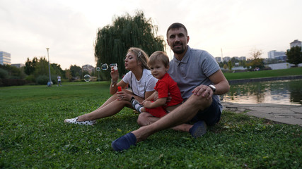 Happy family - dad, mom and little son sitting on grass in the park in summer.