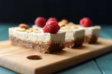 Vegan sugar free dessert. Coconut milk cheesecake bars decorated with raspberries, almonds and coconut flakes on dark background side view