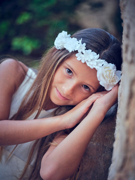 Portrait of little pretty girl wearing white dress flower headband leaning on wall and looking at camera