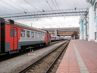 The passenger train at the railway station on a cloudy day. Electric train, wagons, railway platform.