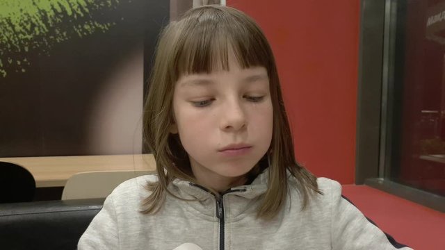 A teenage girl eats French fries for dinner at a fast food cafe.