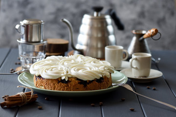 Homemade cake with white rose shaped icing served with coffee on dark background copy space. Still life with natural lighting