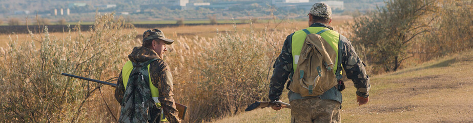 Hunting period, autumn season open. A hunter with a gun in his hands in hunting clothes in the autumn forest in search of a trophy. A man stands with weapons and hunting dogs tracking down the game.	