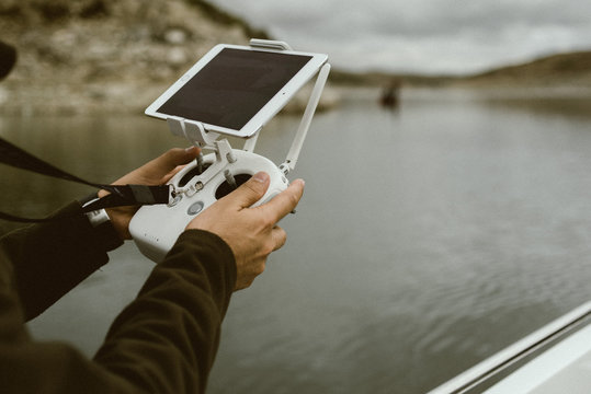 Crop tourist using controller with tablet on stand while sailing on boat in water in cloudy day