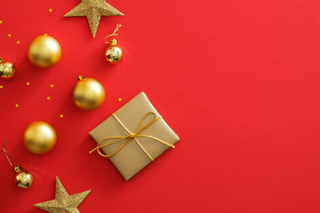 Christmas gold decorations on red background with copy space. Flat lay golden gift box, baubles, stars, glittering confetti. Christmas poster mockup, greeting card template, website header hero