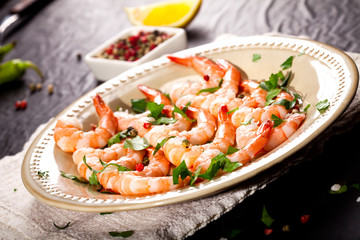 Prawns Shrimps on a plate with lemon, garlic and herbs on black background.