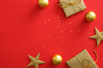 Christmas gold decorations on red background with copy space. Flat lay golden gift box, baubles, stars, glittering confetti. Christmas poster mockup, greeting card template, website header hero
