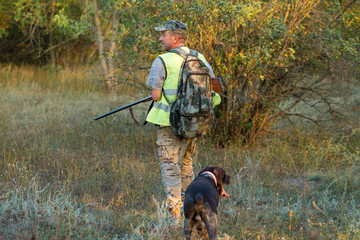 Hunting period, autumn season open. A hunter with a gun in his hands in hunting clothes in the autumn forest in search of a trophy. A man stands with weapons and hunting dogs tracking down the game.	