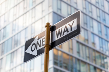 A one way sign with an out of focus building in the background.