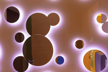 Several round, different-sized mirrors with white illumination are mounted on the wall of the room.