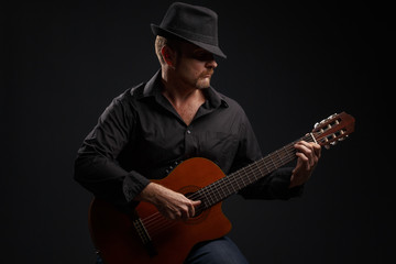 Obraz premium Man in black clothes plays a classic acoustic guitar. Studio photography.