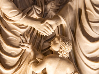 Detail of classical marble sculpture of a boy with a torch watching people shaking hands