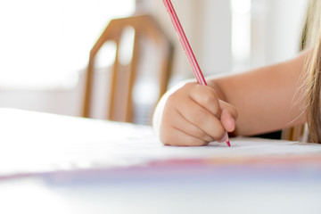 Caucasian child practicing fine motor skills drawing or coloring with crayons on a white sheet