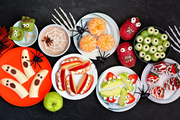 Healthy Halloween fruit snacks. Selection of fun, spooky treats. Top view table scene over a black stone background.