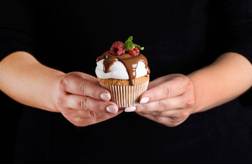 Cupcake with white cream watered with chocolate, rasped with raspberries and mint in the hands of a pastry chef.